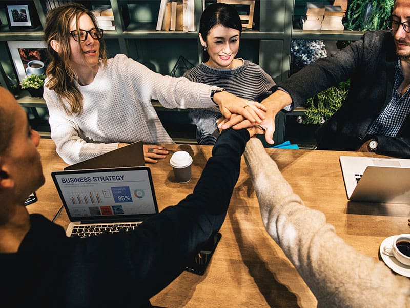 Colleagues joining hands over a table in a team collaboration gesture.