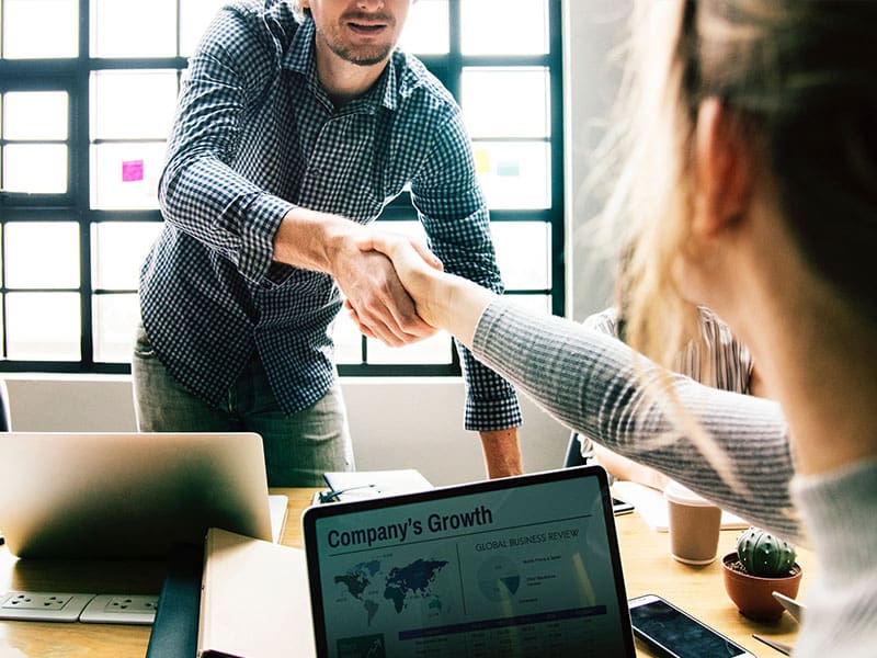 Two colleagues shaking hands in a modern office setting.