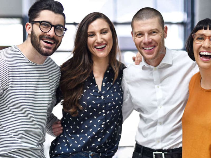Group of four happy friends smiling and posing together indoors.