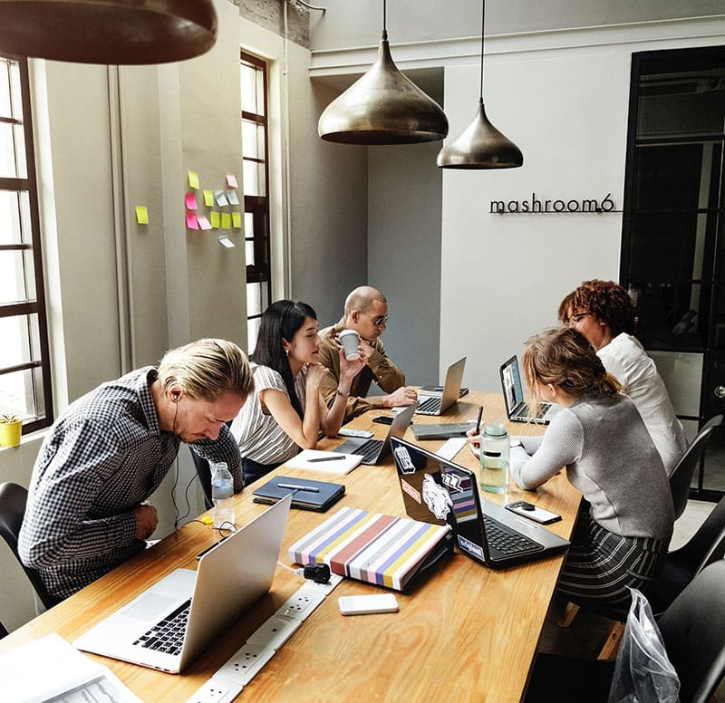 A diverse group collaborating in a modern, well-lit meeting room with laptops and notes.