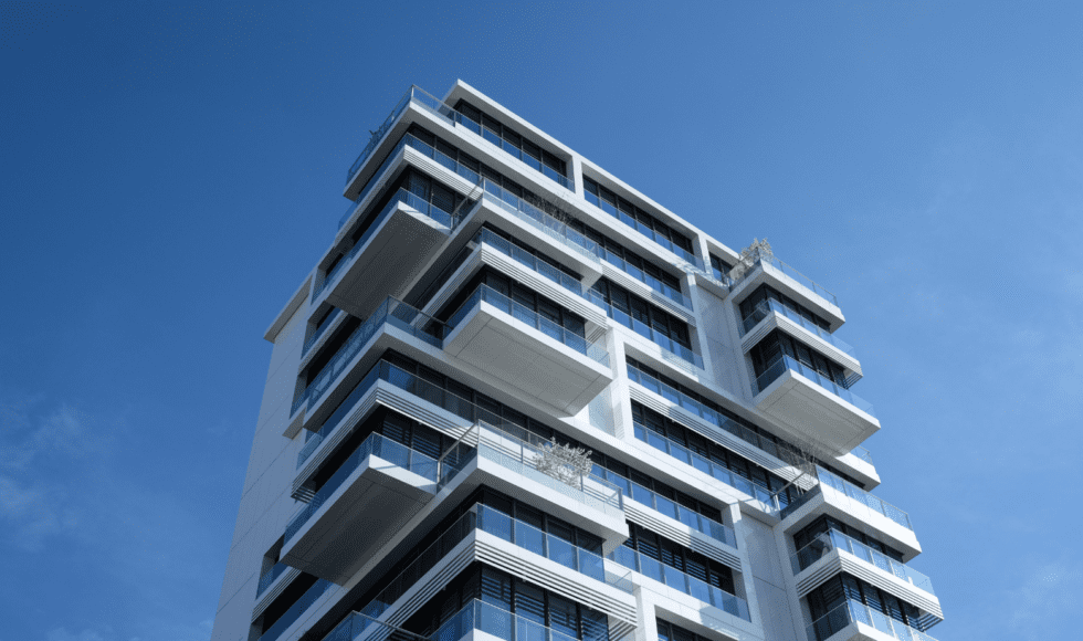 Modern high-rise building with stacked glass balconies against clear blue sky.