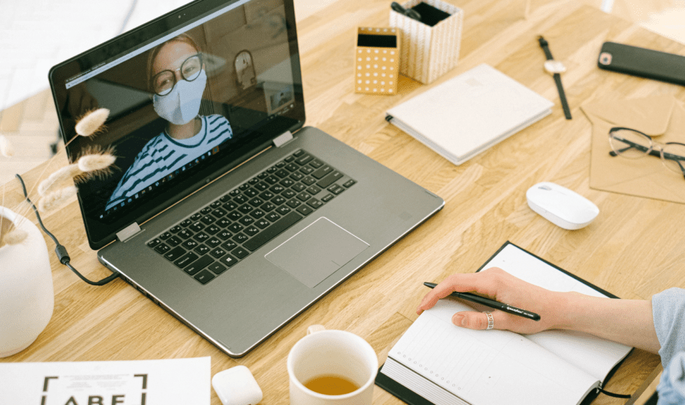 Person taking notes during a video call on a laptop.