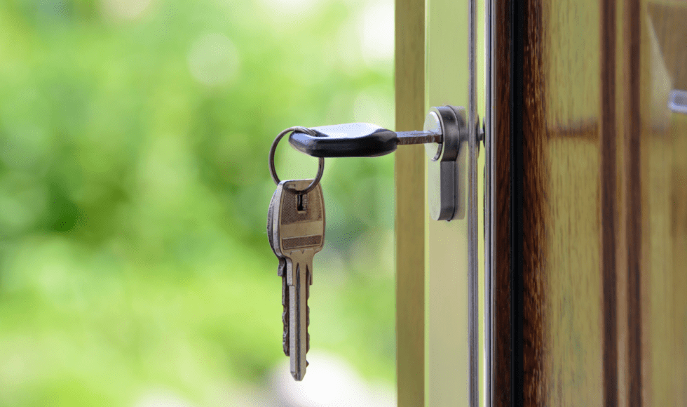 A key inserted in a door lock with a blurred green background.