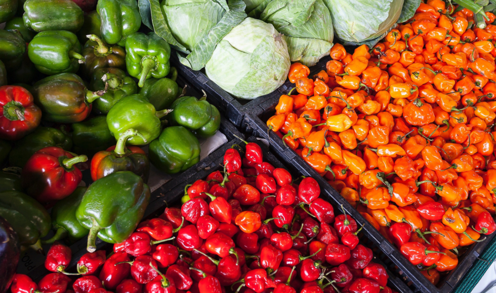 Fresh red, orange, and green peppers displayed in crates at a market.