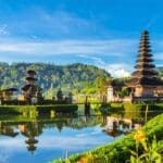Scenic view of a traditional Balinese temple with water reflections and lush hills.