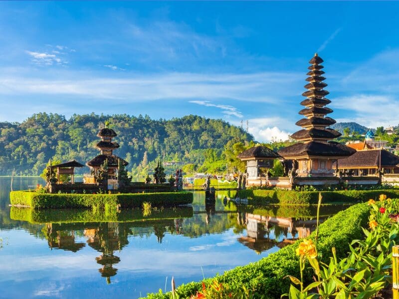 Scenic view of a traditional Balinese temple with water reflections and lush hills.