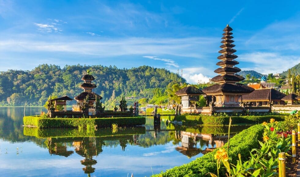 Scenic view of a traditional Balinese temple with water reflections and lush hills.