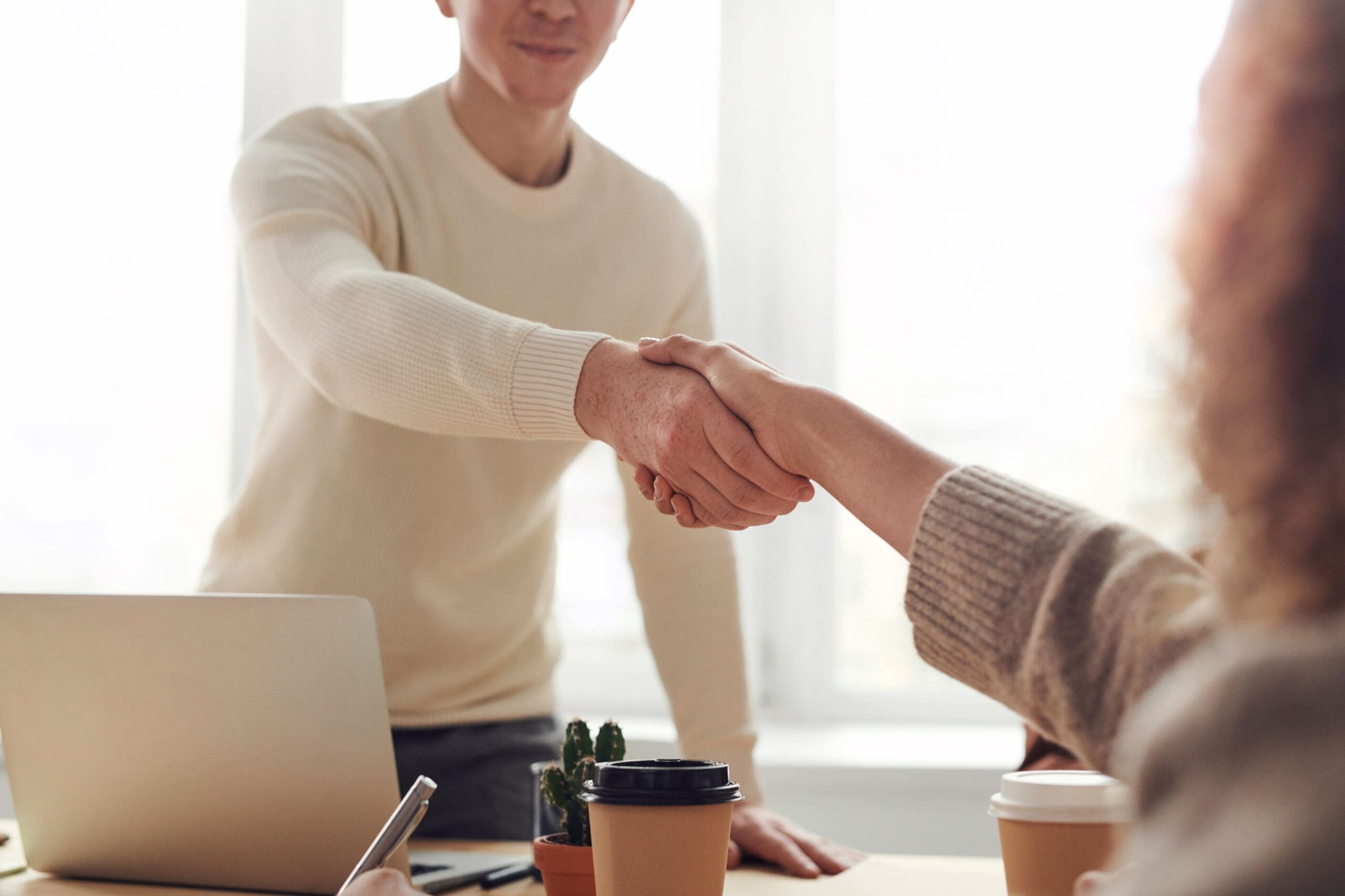 Two people shaking hands in a bright office setting.