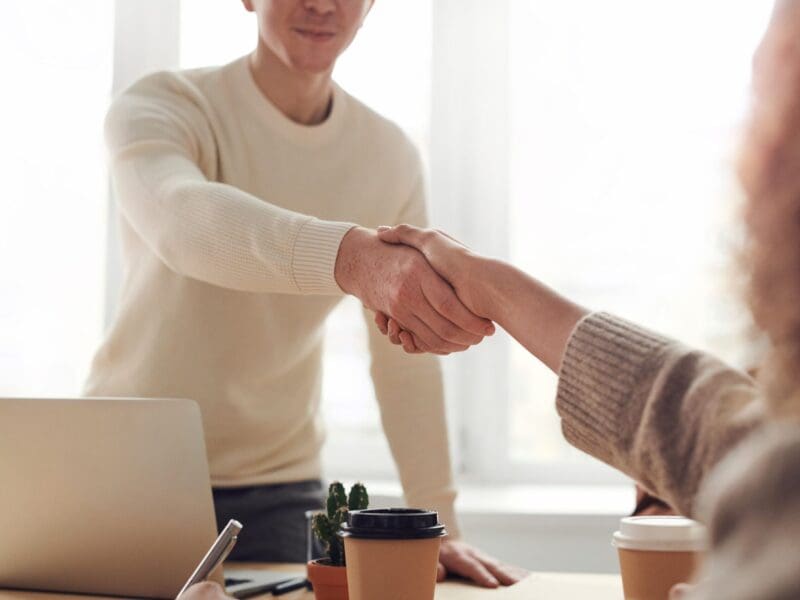 Two people shaking hands in a bright office setting.