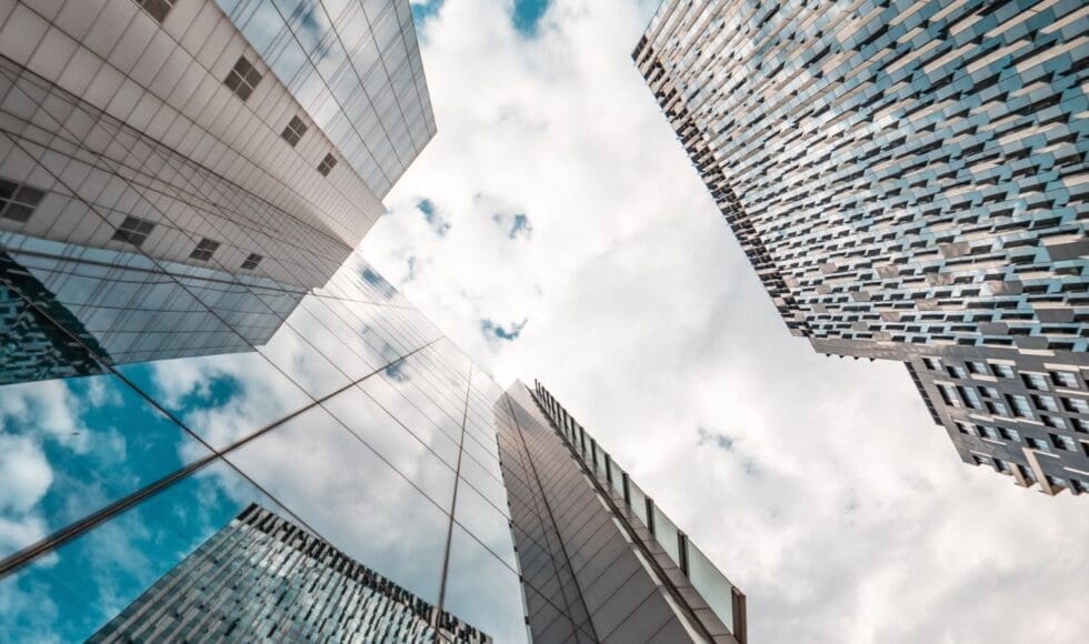 Looking up at tall glass skyscrapers against a blue sky with clouds.