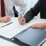 Two professionals reviewing documents and signing papers.