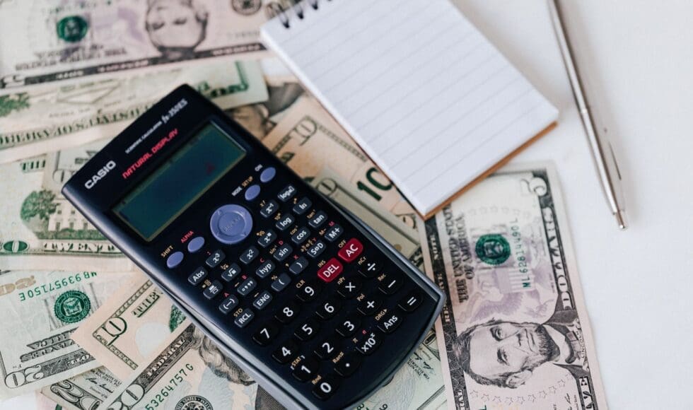 Calculator on dollar bills with a blank notepad nearby.
