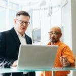 Two businessmen discussing work on a laptop in a modern office.