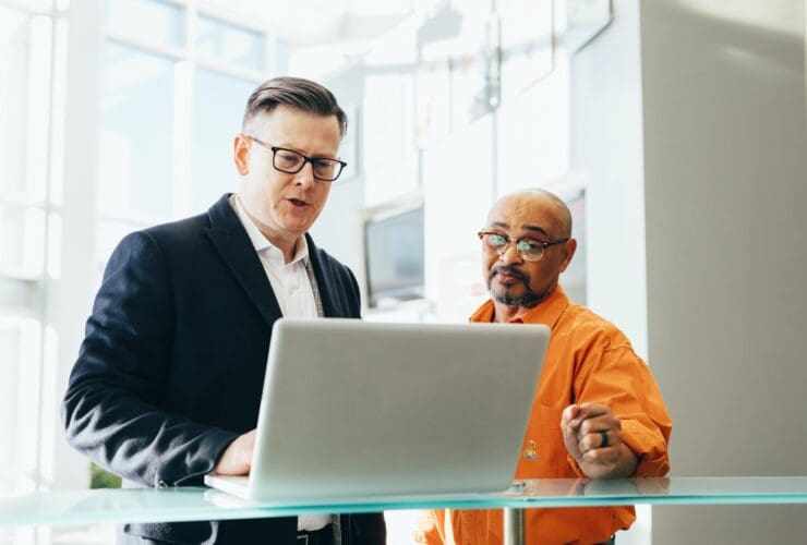 Two businessmen discussing work on a laptop in a modern office.