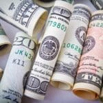 Rolled US dollar bills and a pen on a white surface.