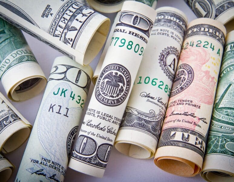 Rolled US dollar bills and a pen on a white surface.