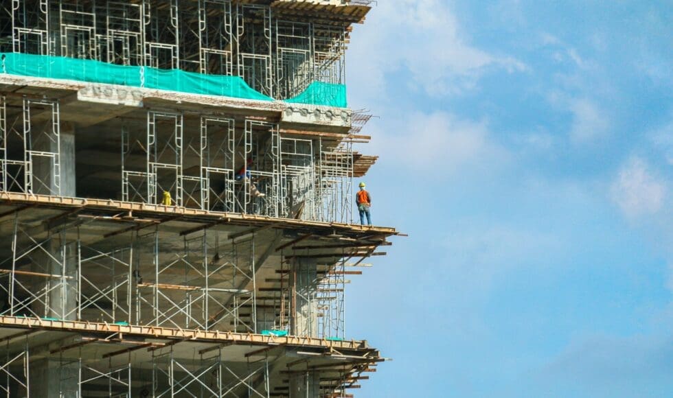 Construction worker standing on scaffolding against blue sky.