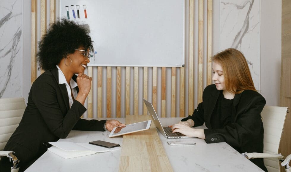 Two women engaged in a discussion at a table with a laptop.
