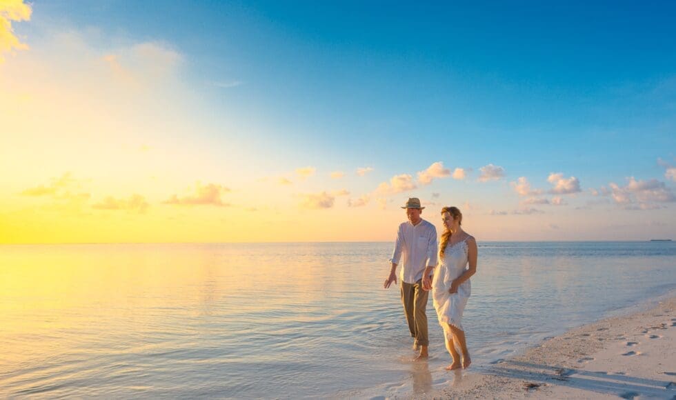 Couple walking hand-in-hand along a serene beach at sunset.