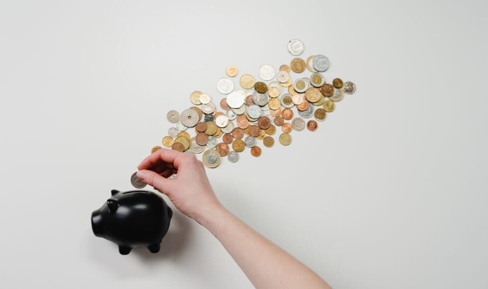 Hand placing coins into a black piggy bank with coins floating away.