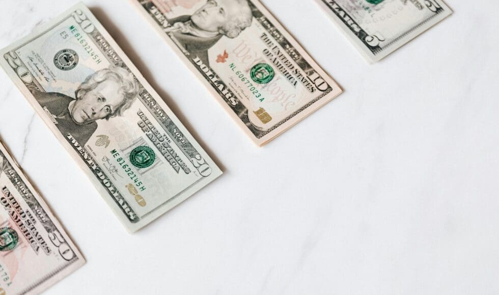 Three US dollar bills on a white surface.