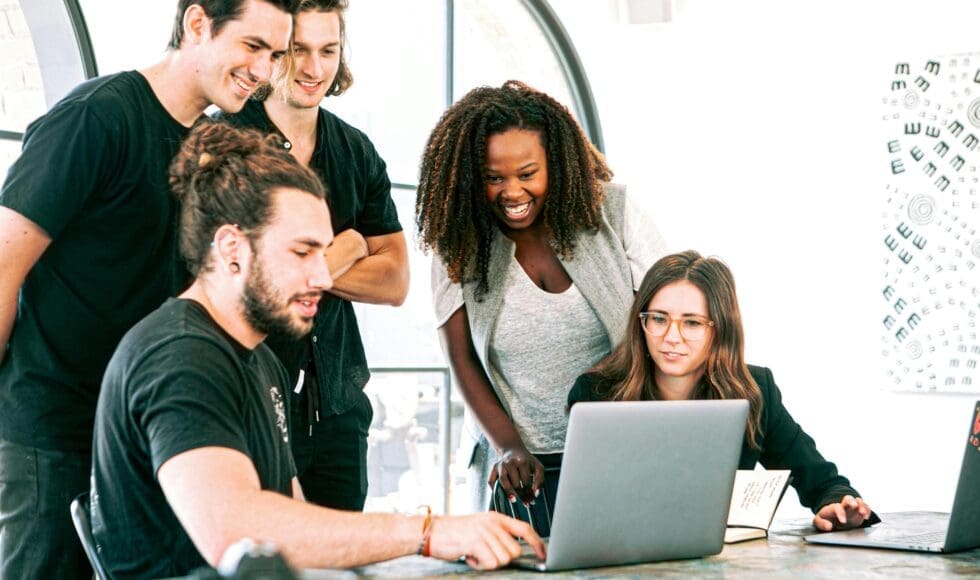 A diverse group of five young professionals collaborating around a laptop.