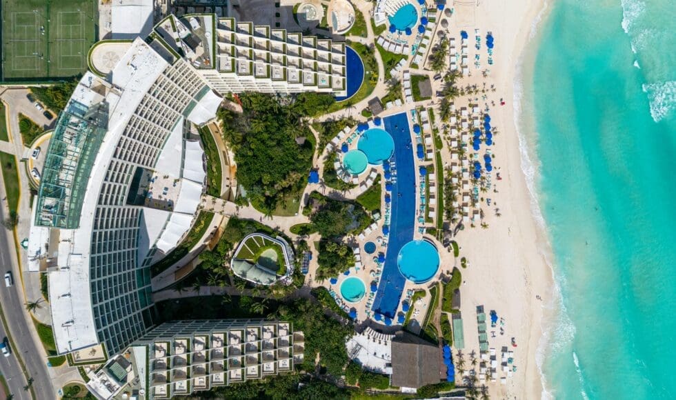 Aerial view of a beachfront resort with pools and sandy beach.