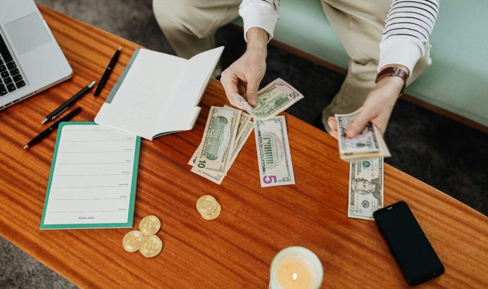 Person counting cash bills and coins on a wooden table.