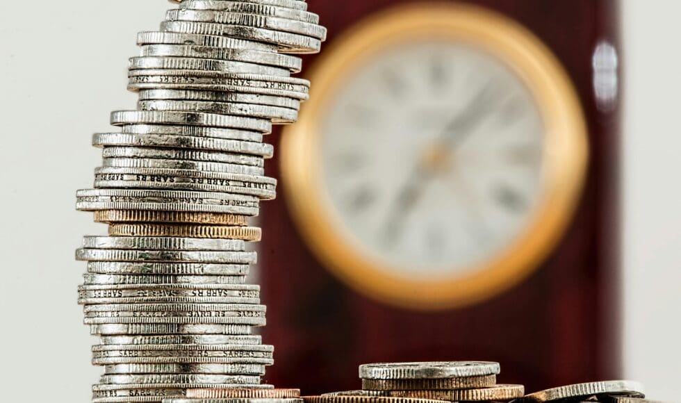 Stack of coins with a blurred clock in the background.