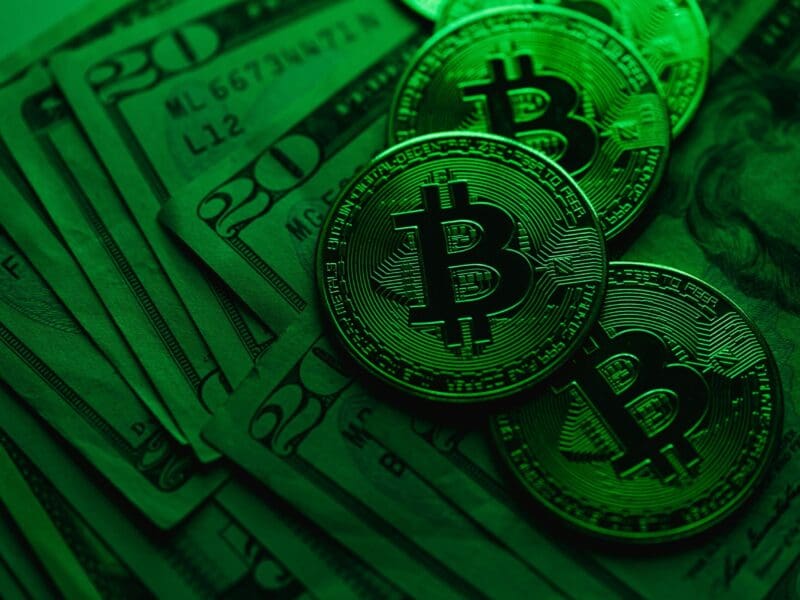 Bitcoin coins on US dollar bills with a green overlay.