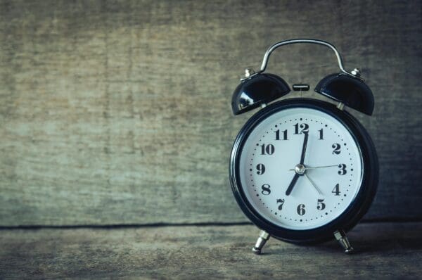 A classic black alarm clock shows the time as 6:15 on a wooden surface.