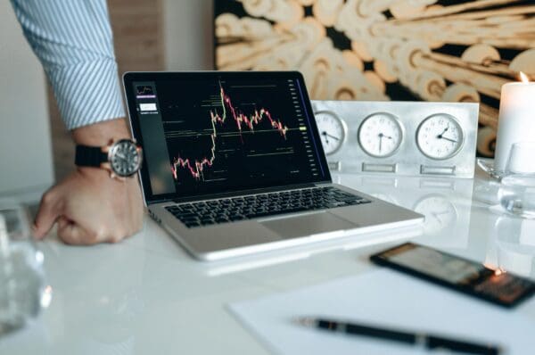 Laptop displaying a stock market graph on a desk with clocks and documents.